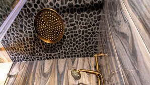 Une salle de bain avec un mur en pierre, une douche dotée d’un pommeau doré et un plancher en bois.