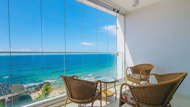Ein Balkon mit Korbstühlen und einem kleinen Tisch, mit Blick auf einen Strand und das Meer.
