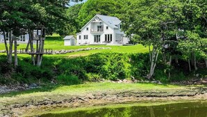 Una grande casa bianca con un balcone, immersa nel verde e con uno stagno.