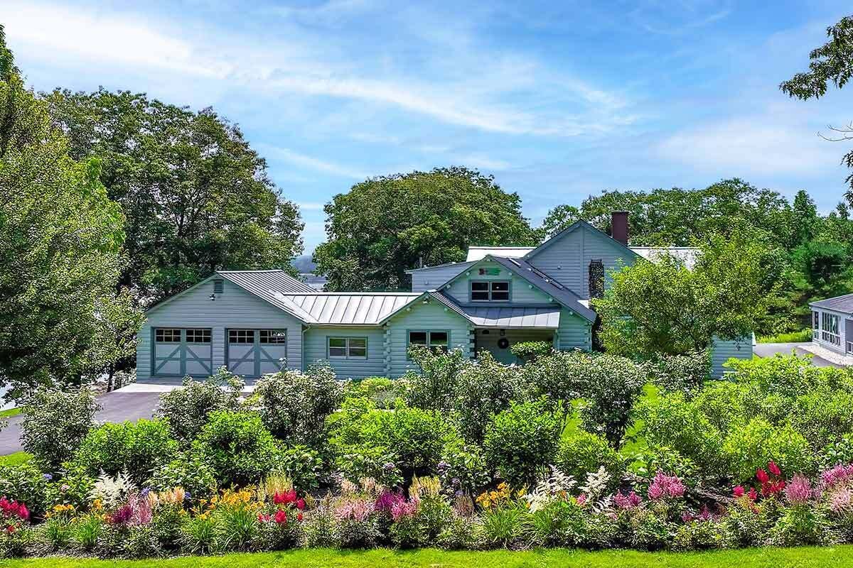 Ein hellblaues Haus mit Garage, umgeben von üppiger Vegetation und bunten Blumen.