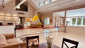 Un'ampia hall d'hotel con soffitto alto, un modellino di una barca a vela, una reception e un'area relax con tavolo e sedie.