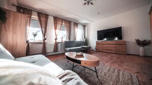 A modern living room with a sofa, a coffee table, a TV, and a wooden cabinet. - FlexHome Stylish vacation apartment (Lippstadt)