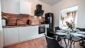 A modern kitchen with white cabinets, a wooden countertop, a black range hood, and a dining area with a table set for two. - FlexHome Stylish vacation apartment (Lippstadt)