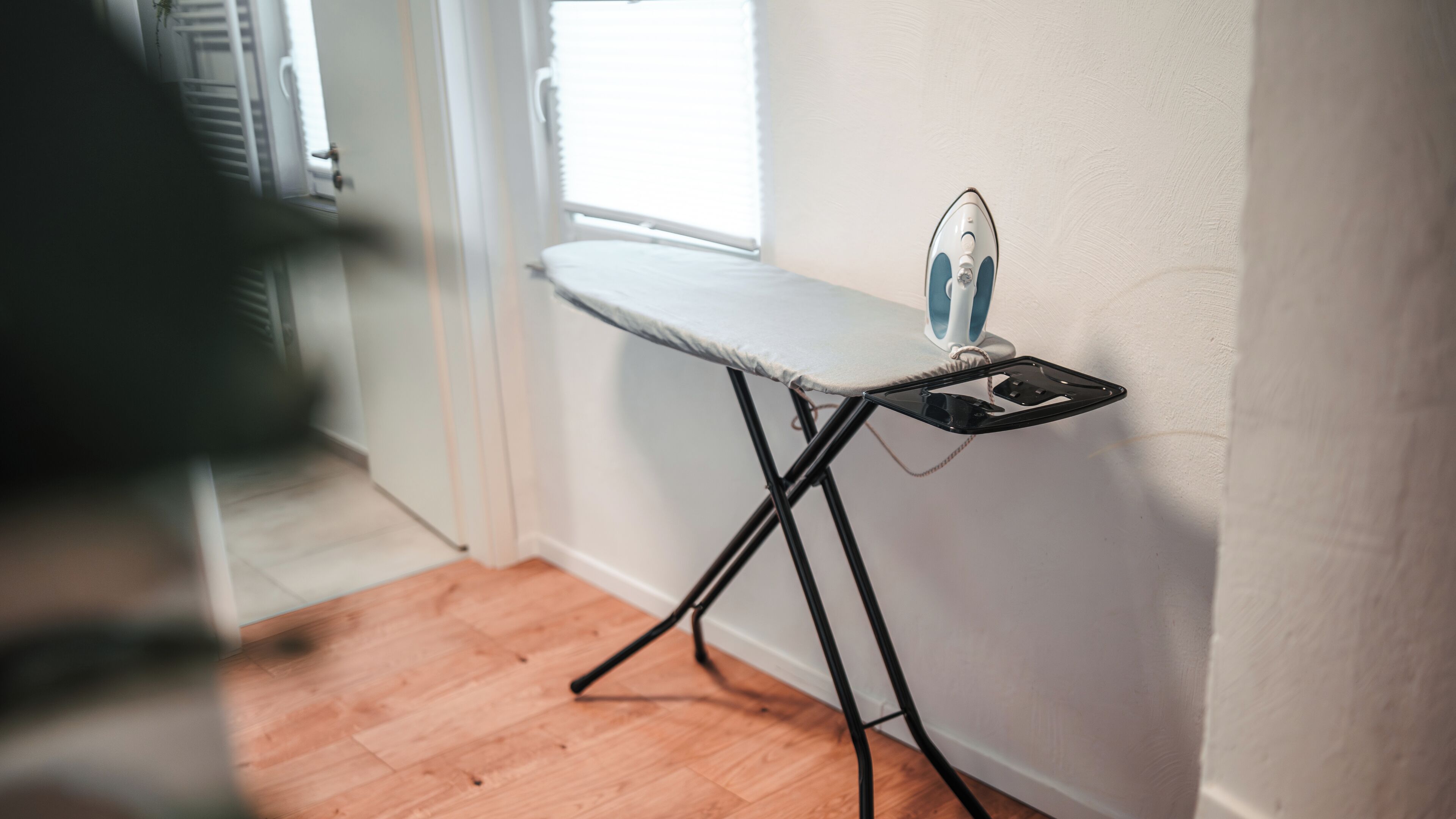 A compact ironing station with a foldable table and an iron, positioned against a wall in a room with wooden flooring.