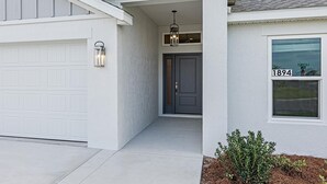 Une maison moderne à l’extérieur blanc, avec une porte de garage, une porte d’entrée et une fenêtre portant le numéro 1894.