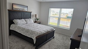 Une chambre à coucher avec un lit, une table de chevet, une lampe, une fenêtre donnant sur un beau paysage et un tableau au mur.