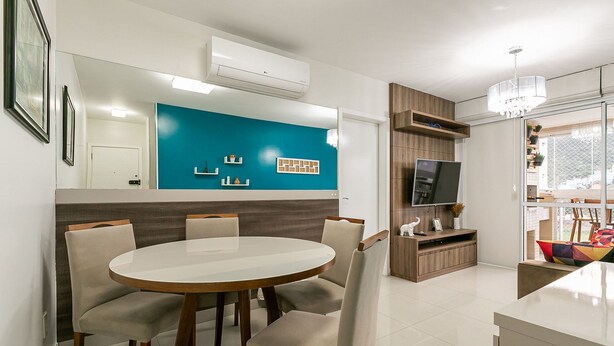 A modern dining area with a round table and six chairs, a blue accent wall, and a TV on a wooden stand. - 50" Smart TV | 500 meters from UFSC #TRINA03D (Florianópolis)
