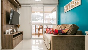 A modern living room with a flat-screen TV, wooden entertainment unit, and a sofa with colorful cushions. - 50" Smart TV | 500 meters from UFSC #TRINA03D (Florianópolis)