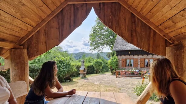 Un pavillon en bois, doté d’une table et de bancs, qui offre une vue sur un jardin et un bâtiment avec une cheminée.