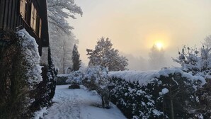 Une cabane en bois dont l’extérieur est recouvert de neige, entourée d’arbres et de buissons chargés de neige.