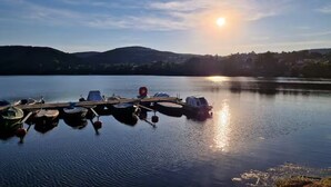 Un lac paisible où des bateaux sont amarrés à un quai, entouré de collines et surplombé d’un ciel dégagé.