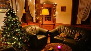 Un salon chaleureux avec un sapin de Noël, des fauteuils en cuir, une lampe et une petite table.
