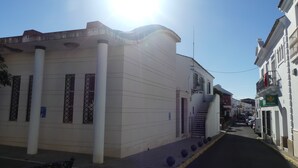 A narrow street with buildings on either side, including a white building with large windows and a staircase leading to a second floor. - Casa La Peña (Pet friendly) 1 min drive from the beach! (La Redonela)