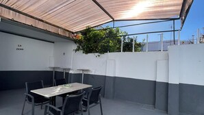 An outdoor patio with a table and chairs, a pergola providing shade, and a white wall with a black baseboard. - Casa La Peña (Pet friendly) 1 min drive from the beach! (La Redonela)