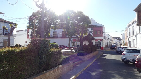 A street with parked cars, a building with a red and white facade, and a tree in the foreground.