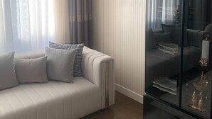 A modern living room with a white sofa, a glass cabinet, and a large window with sheer curtains. - YİLDİRAY YİLMAZ GENEL TRADİNG FZ-LLC (Ras Al Khaimah)