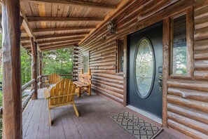 Une cabane en rondins avec un porche en bois, un banc et une porte ornée d’un panneau de verre décoratif.