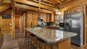 A log cabin kitchen with wooden cabinets, a granite countertop, a stainless steel refrigerator, and a bar stool.