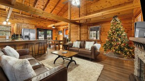 A cozy cabin interior with a wooden ceiling, a dining area, a living room with a leather couch, and a Christmas tree.