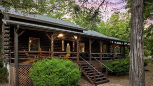A rustic log cabin with a porch, outdoor seating, and a staircase leading to the entrance.