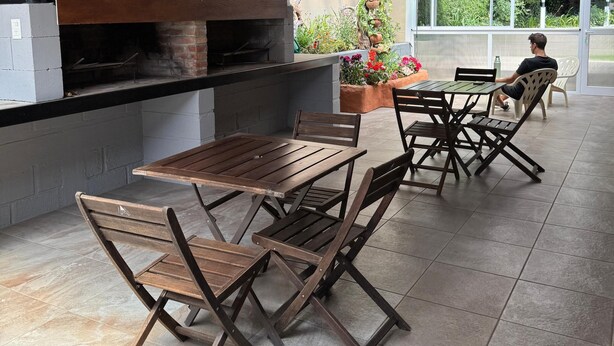 Eine Terrassenausstattung im Freien mit Kamin aus Backstein, einem Holztisch und -stühlen sowie Blick ins Grüne durch ein großes Fenster.
