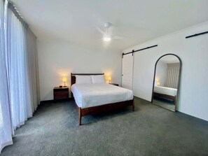 A bedroom with a bed, a nightstand, a ceiling fan, a mirror, and a door.