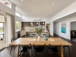 Una cocina moderna con una isla central, iluminación colgante y una zona de comedor con mesa de madera y sillas negras.