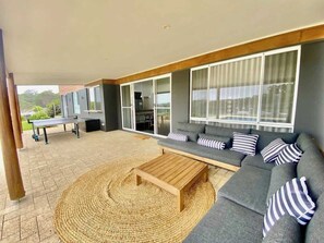 Un espacio exterior moderno con un sofá, cojines, una mesa de centro de madera y un tapiz tejido.