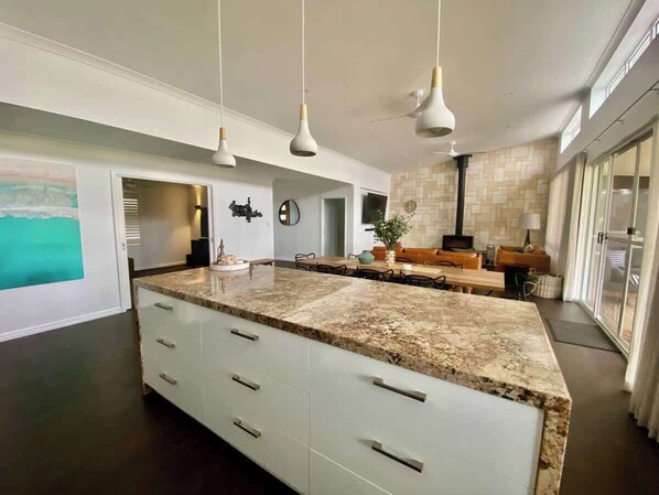 A modern kitchen with a large island, pendant lighting, and a view to the outside.