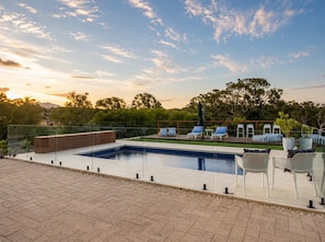 Une piscine rectangulaire avec une barrière en verre, entourée de chaises longues et d’une terrasse en bois.