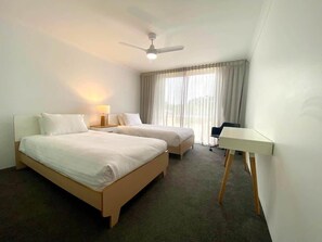 Una habitación de hotel con dos camas, un escritorio, un ventilador de techo y una ventana con cortinas.