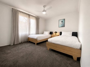 Una habitación de hotel con dos camas individuales, un ventilador de techo, una mesita de noche con una lámpara y un cuadro en la pared.