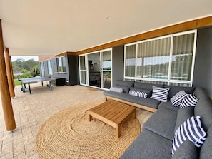 Un espacio exterior moderno con un sofá, una mesa de centro de madera y una mesa de tenis.