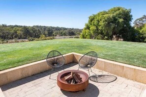 A patio with a fire pit and two chairs, overlooking a grassy field and trees.