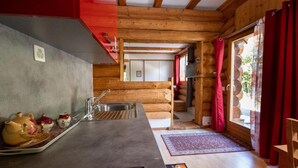 A log cabin interior with a kitchen area, a dining table, and a red curtain. - Studio with terrace (7 minutes from Vercorin) (Chalais)