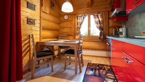 A wooden cabin interior with a dining table, chairs, a red kitchen, and a window with curtains. - Studio with terrace (7 minutes from Vercorin) (Chalais)