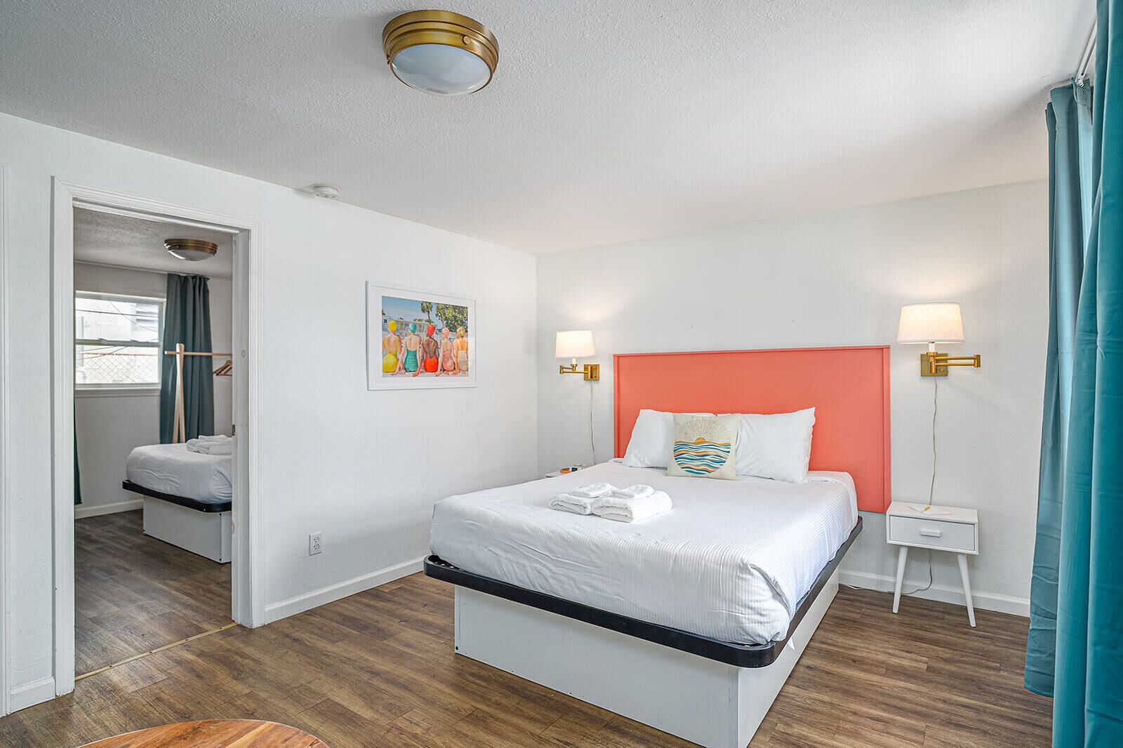 A hotel room with a bed, bedside tables, a nightstand, a painting, and a ceiling light.