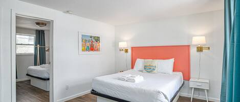 A hotel room with a bed, bedside tables, a nightstand, a painting, and a ceiling light.