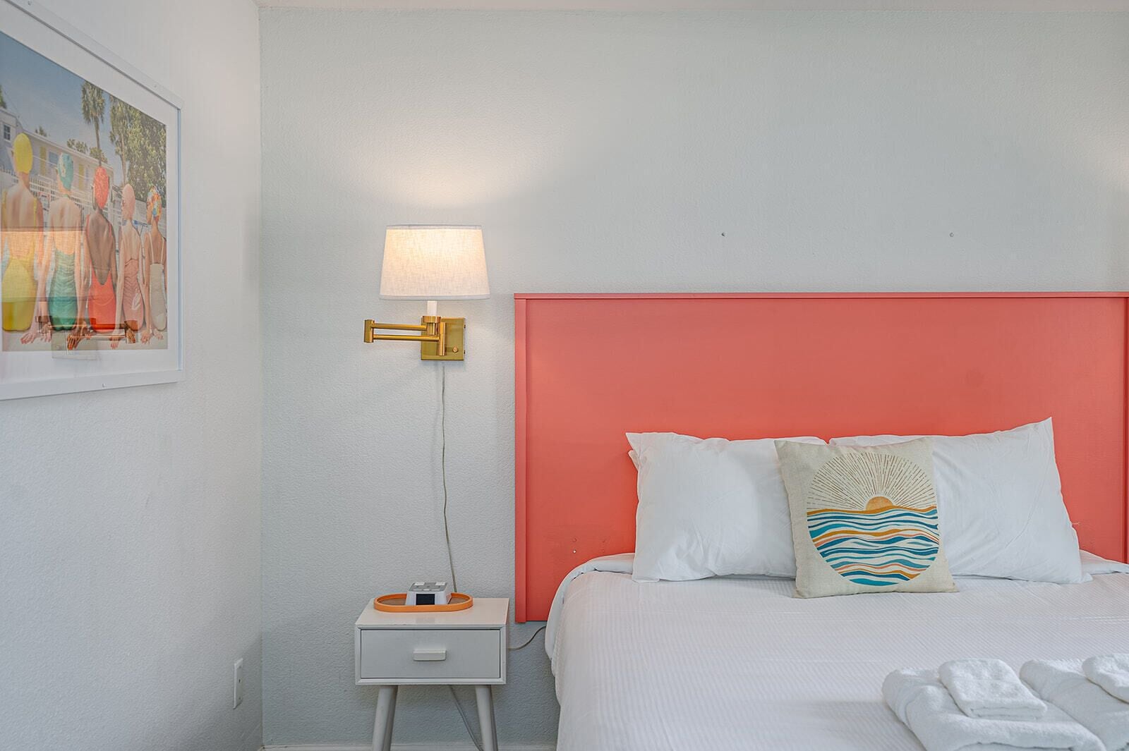 A hotel room with a bed, a nightstand, a lamp, and a painting on the wall.