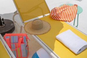 Una silla de playa amarilla con un sombrero de paja, un bolso de playa a rayas y una toalla blanca.