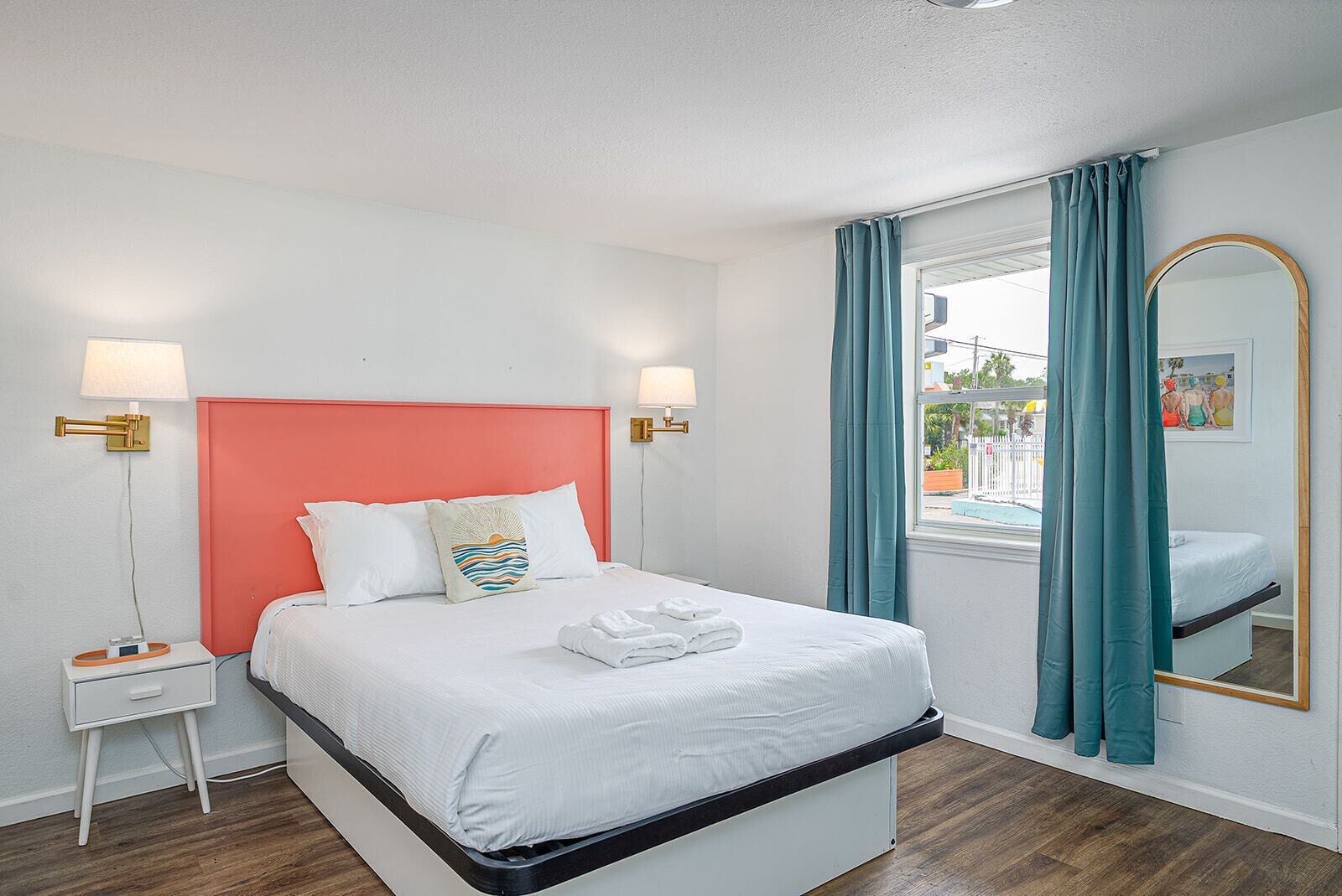 Une chambre d’hôtel avec un lit, des tables de chevet, un miroir et une vue sur l’extérieur.
