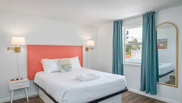 A hotel room with a bed, nightstands, a mirror, and a view of the outside.