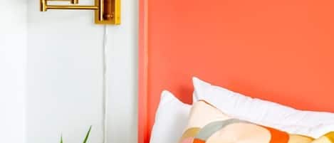 A bed with a white comforter, a colorful pillow, and a small potted plant on a nightstand.