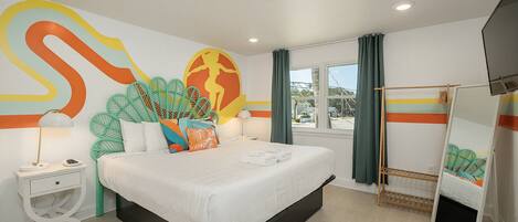 A modern hotel room with a large bed, a window with curtains, a flat-screen TV, and a unique wall mural.