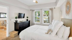 A bedroom with a bed, a ceiling fan, a TV, a dresser, and a window with curtains.
