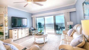 Un salon spacieux doté d’un ventilateur de plafond, d’un grand téléviseur à écran plat, d’un canapé, d’une table basse et d’un balcon avec des chaises.