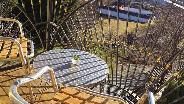 Ein Sitzbereich im Freien mit Metallgestell, einem Holztisch und Stühlen mit Blick auf eine gebirgige Landschaft.