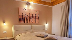 Ein Schlafzimmer mit Holzboden, einem Bett mit gemustertem Bettbezug, Nachttischlampen und einem Wandbild.
