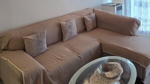 Ein Wohnzimmer mit einem beigen Sofa, einem Glastisch, einer Holzboden und einer Wanduhr.