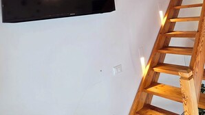 Eine Holztreppe führt zu einer Zwischenebene, auf der ein Flachbildfernseher an der Wand befestigt ist.